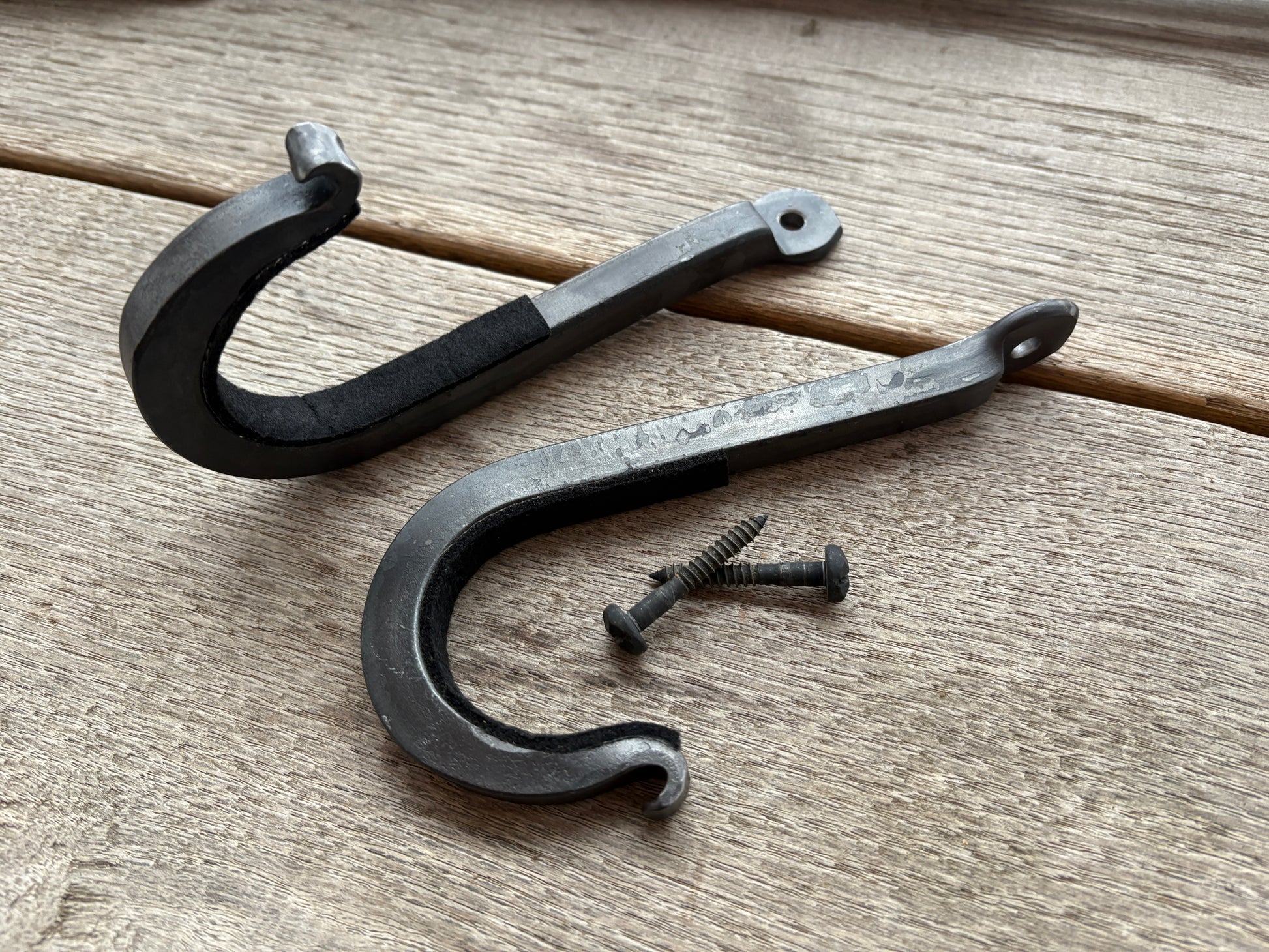 Two black metal hooks with a screw on a wooden surface