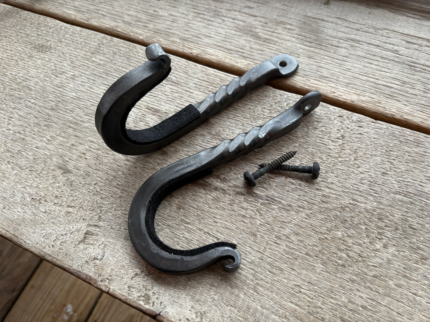 Two black metal hooks with a screw on a wooden surface