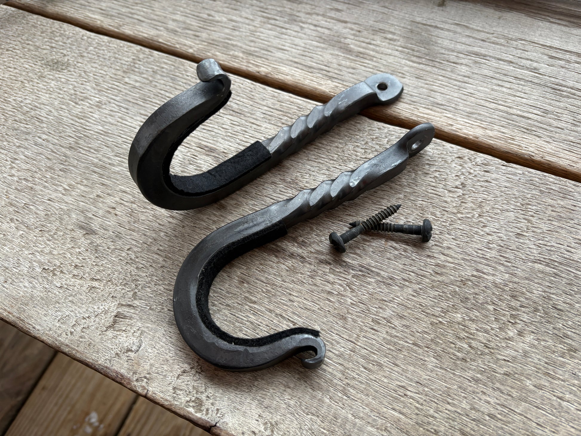 Two black metal hooks with a screw on a wooden surface